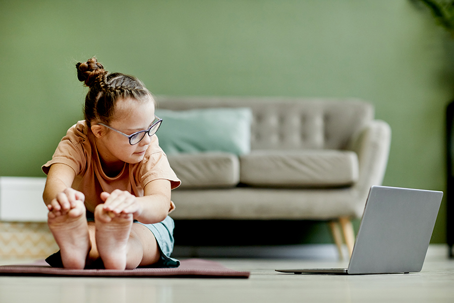 Front view of girl with down syndrome doing stretching exercises while enjoying exercise at home via online class